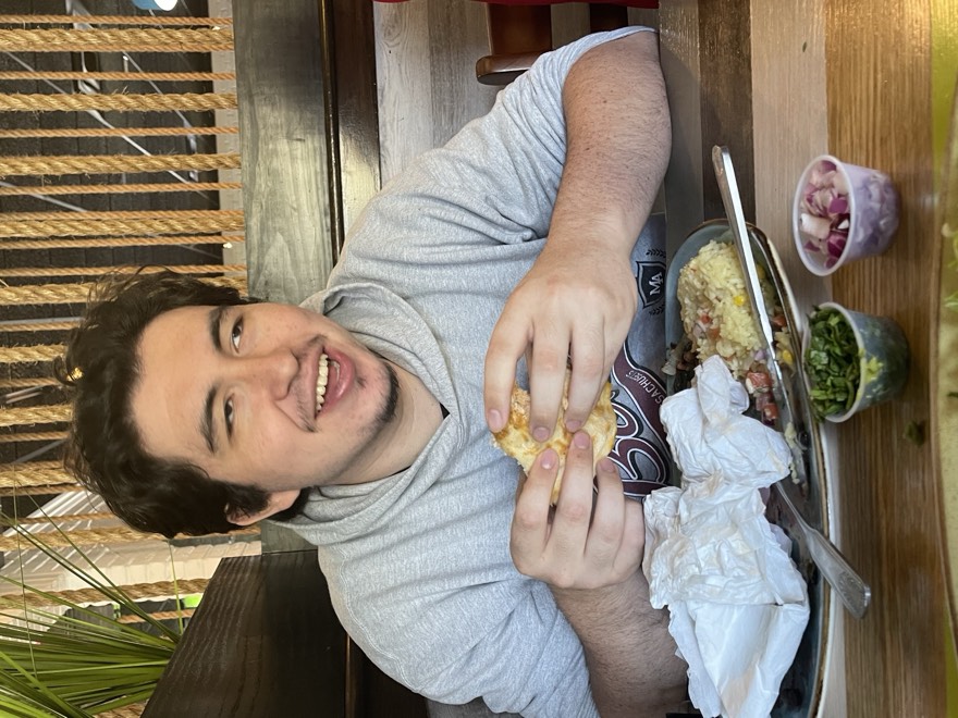 Adam smiling at a restaurant table holding a taco