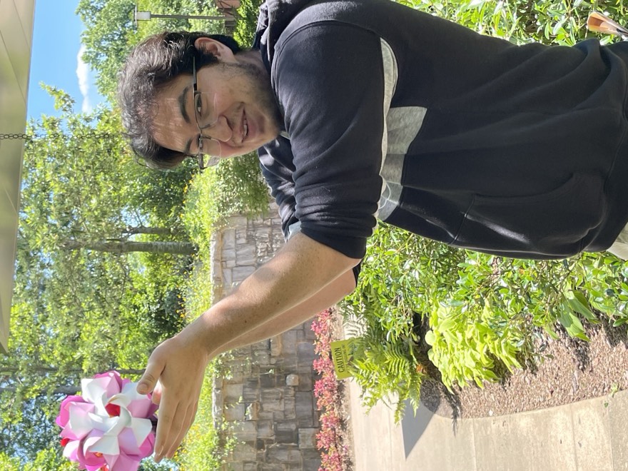 Adam holding a pink and white flower up at arm's length outdoors