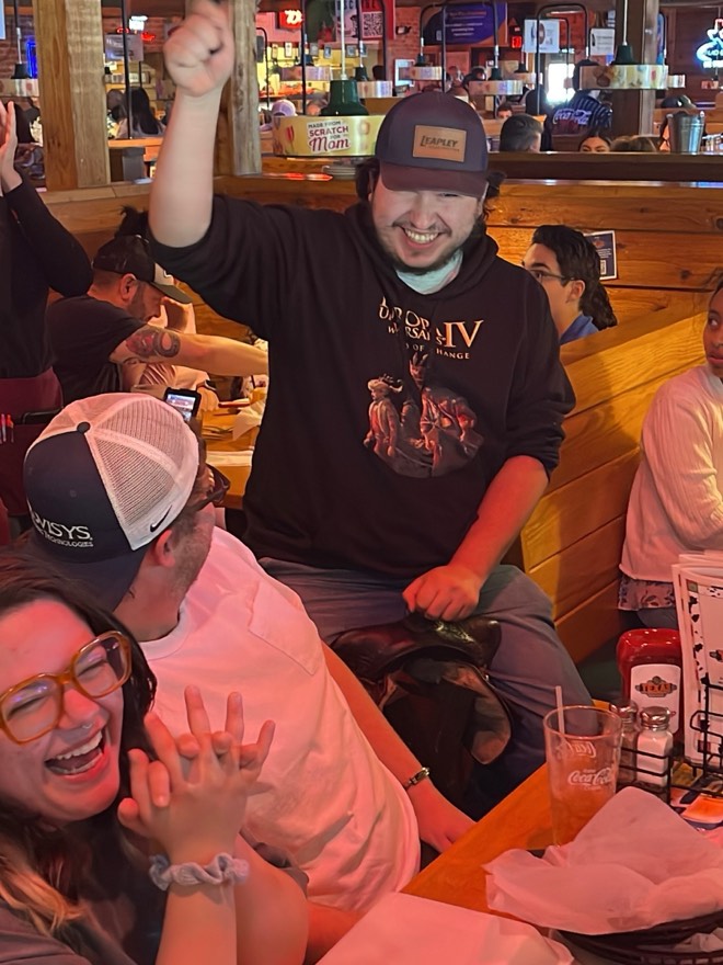 Adam with one arm raised celebrating at a restaurant table